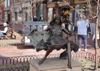 Bronze statue of a woman sitting on a swing in a public square.