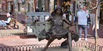 Bronze statue of a woman sitting on a swing in a public square.