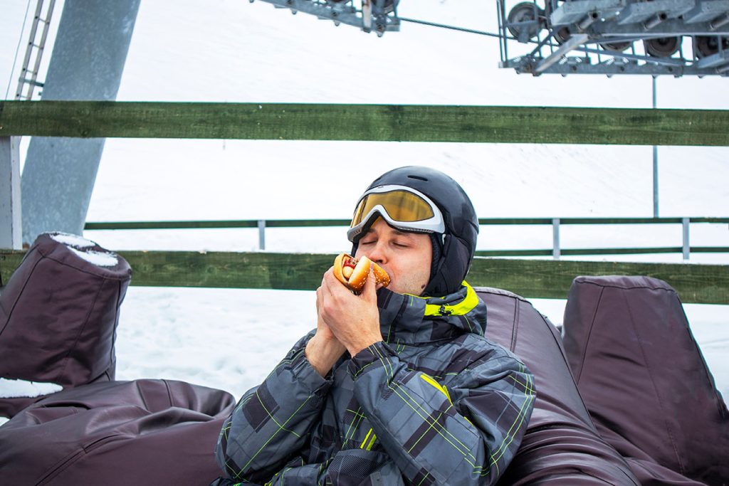 Skier in winter gear enjoying a hot dog at a snowy ski resort