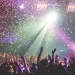 Crowd enjoying a live concert with colorful confetti and stage lights.