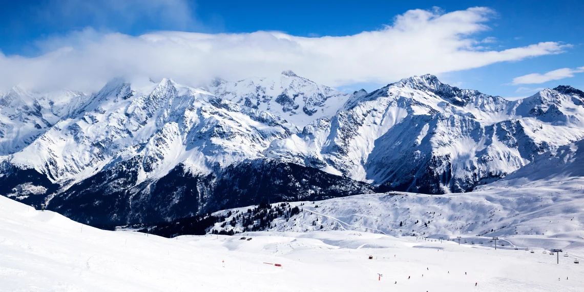 Winter mountain landscape with people enjoying outdoor winter activities, snow-covered peaks, and clear skies.