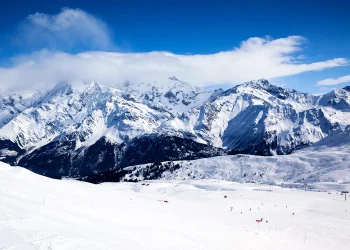 Winter mountain landscape with people enjoying outdoor winter activities, snow-covered peaks, and clear skies.