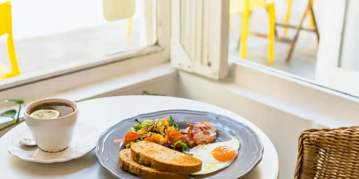 Breakfast plate with fried egg, bacon, salad, and toast next to a cup of tea