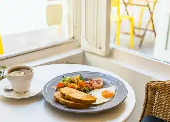 Breakfast plate with fried egg, bacon, salad, and toast next to a cup of tea
