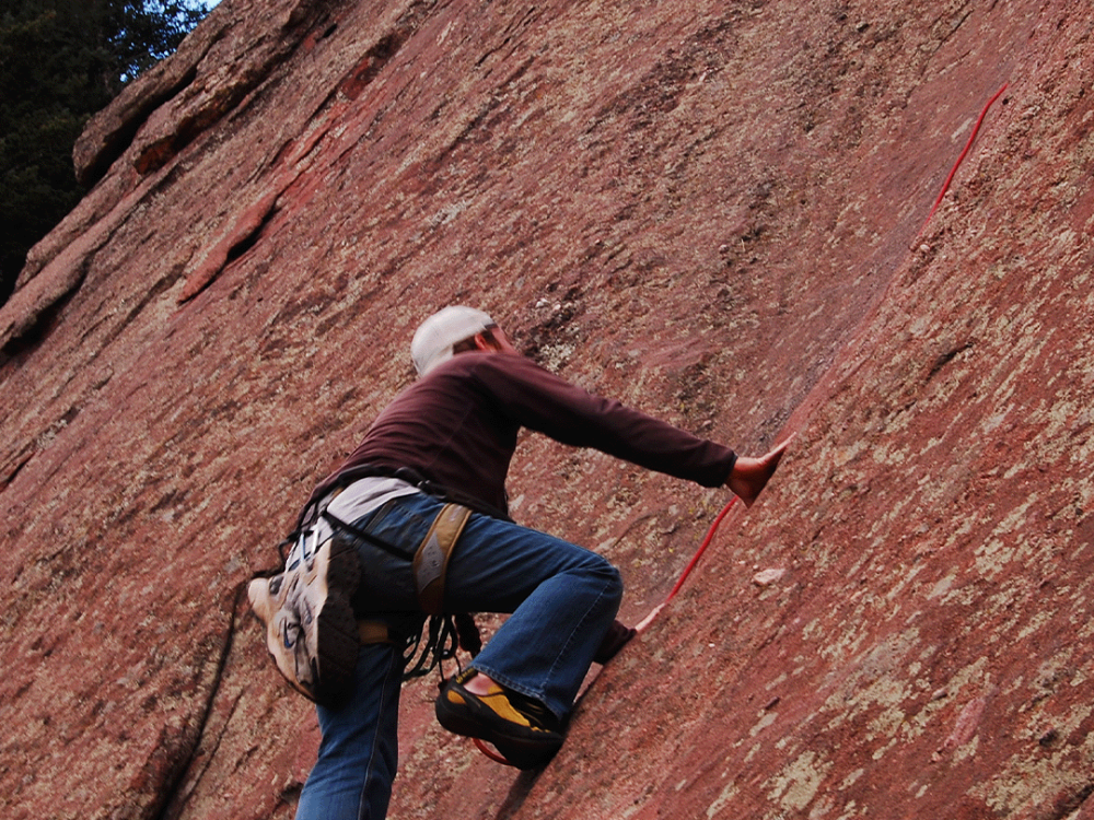 Rock climber scaling the red sandstone Flatirons in Boulder
